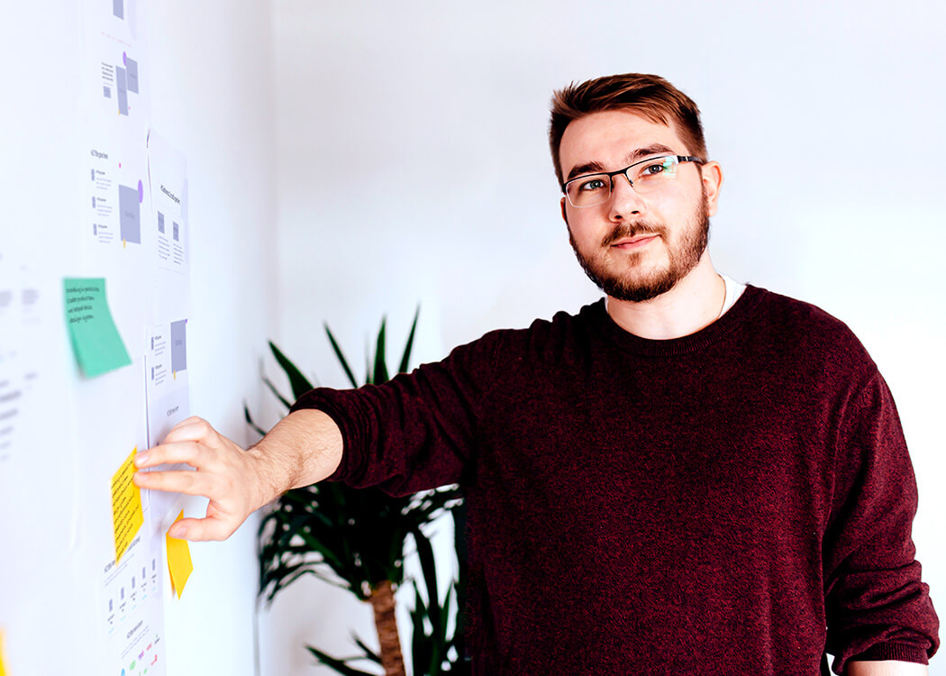 Mirek looking happily at the camera whilst pushing a yellow post-it note with unknown content written on